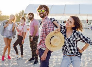 Summer lifestyle image.  Group of beat friends posing on the beach. Casual   look. Warm soft sunset colors. Beardy man in sunglasses.