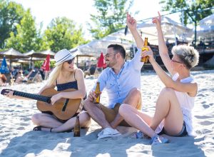 A picture of happy people with a guitar and beer at a beach
