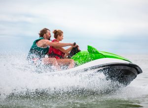 young people having fun driving on high speed on water scooter, man and woman on summer vacation, friends doing active sport